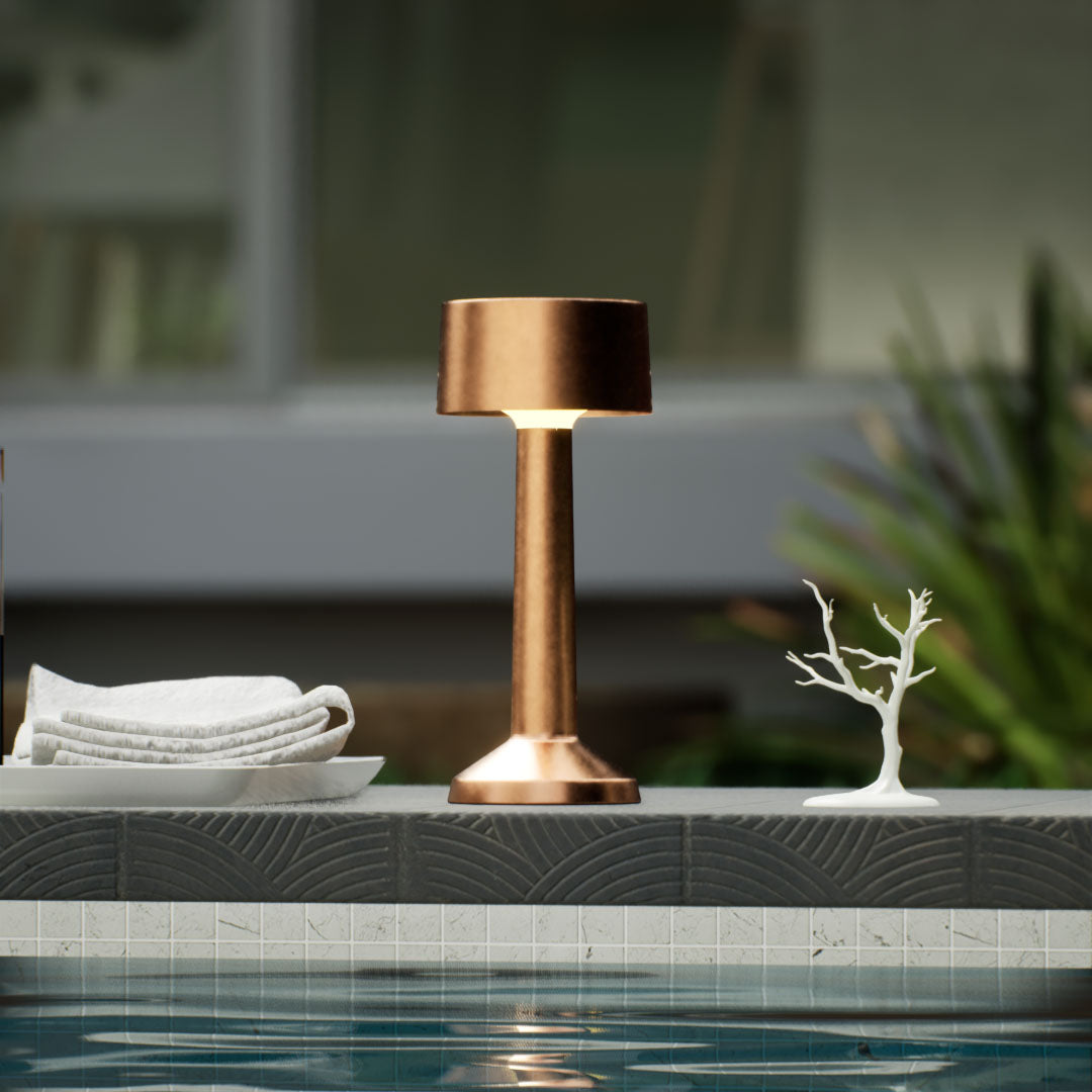 Copri | Cordless Table Lamp | Iron, Acrylic | Bronze color of product | Warm light on | Close-up distance to lamp | Near outdoor pool | Noon