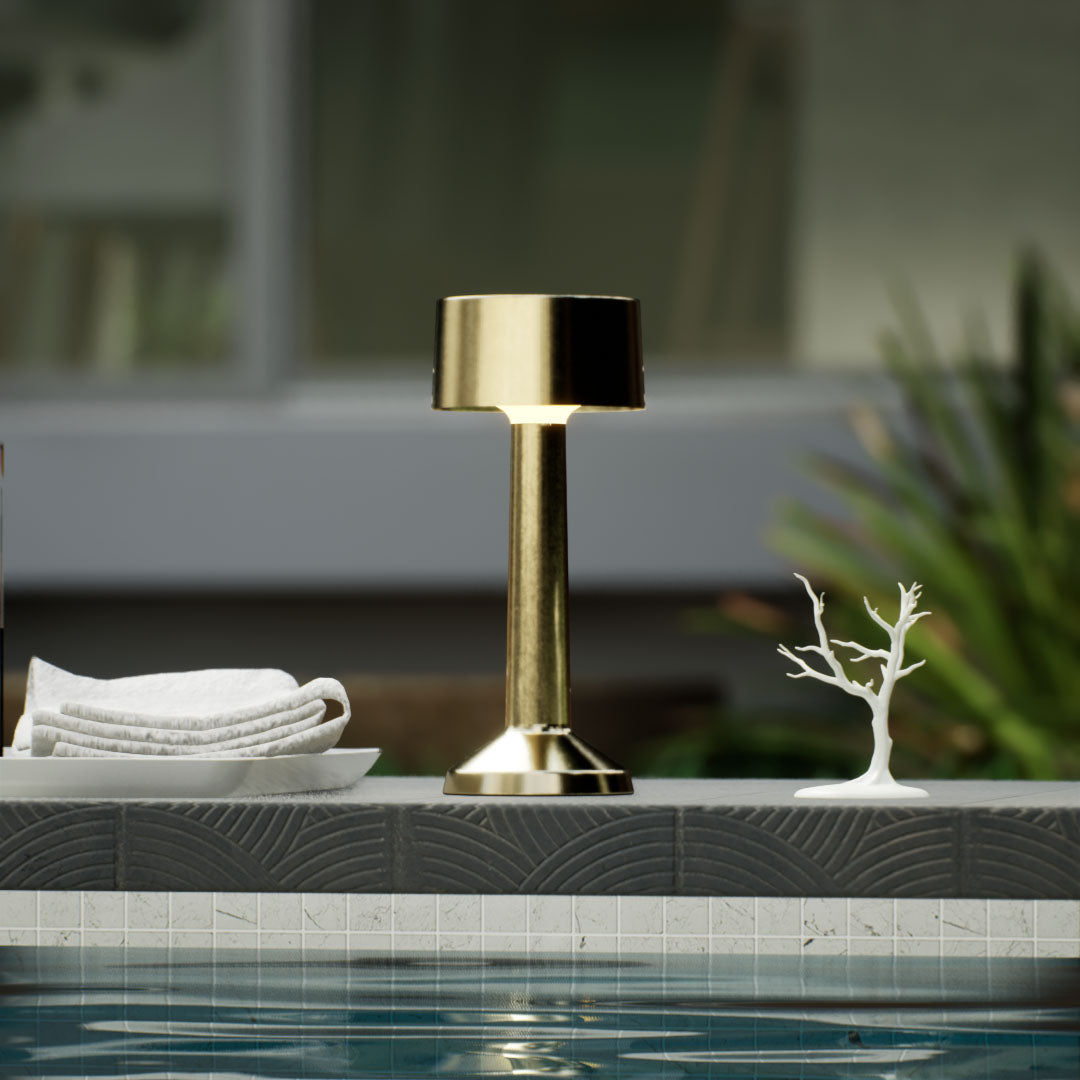 Copri | Cordless Table Lamp | Iron, Acrylic | Gold color of product | Warm light on | Close-up distance to lamp | Near outdoor pool | Noon