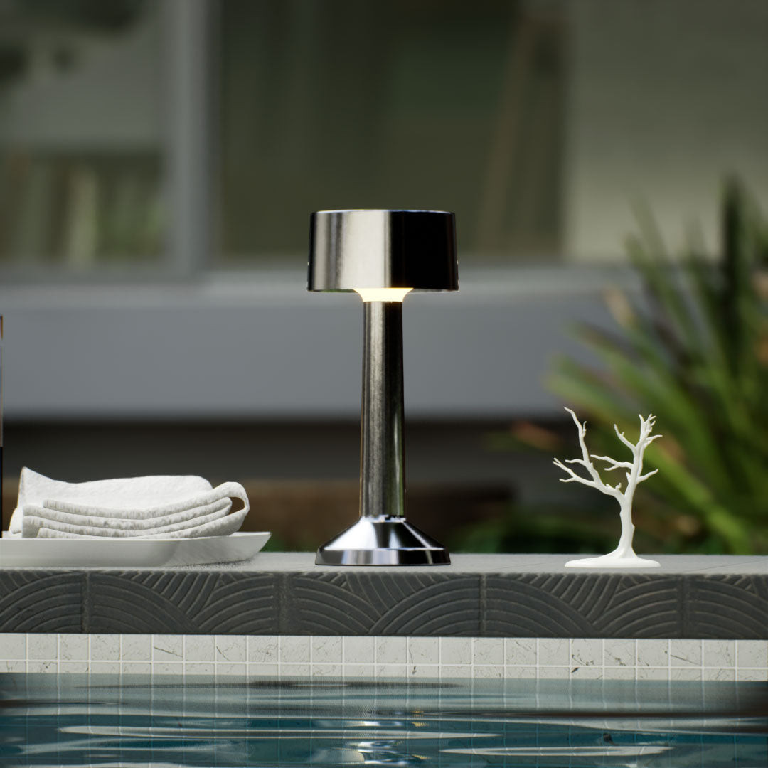 Copri | Cordless Table Lamp | Iron, Acrylic | Silver color of product | Warm light on | Close-up distance to lamp | Near outdoor pool | Noon